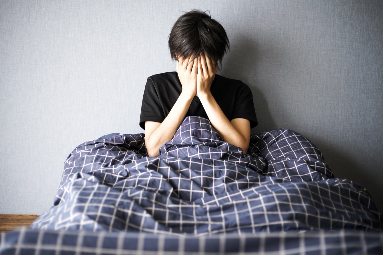 朝、ベッドの上で顔を覆って座り込む男性
