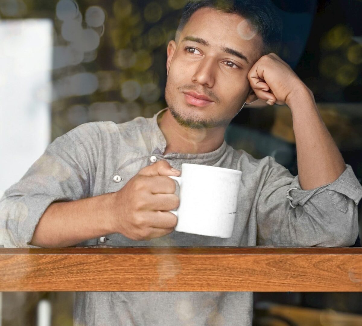 窓辺でマグカップを手に外を眺める男性