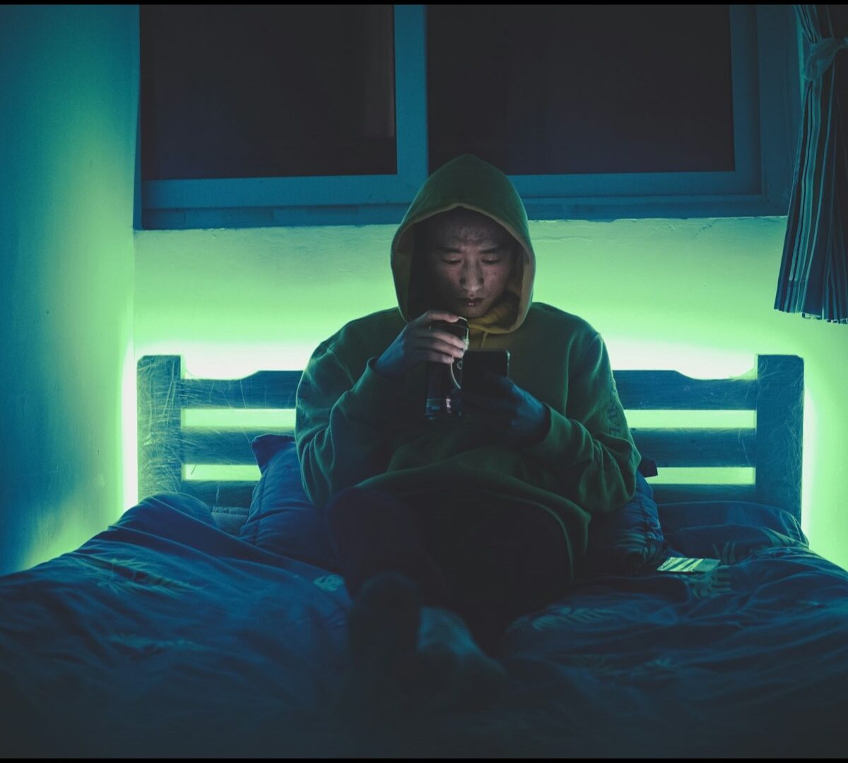 夜のベッドでスマートフォンを見る男性