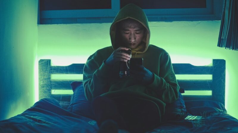 夜のベッドでスマートフォンを見る男性